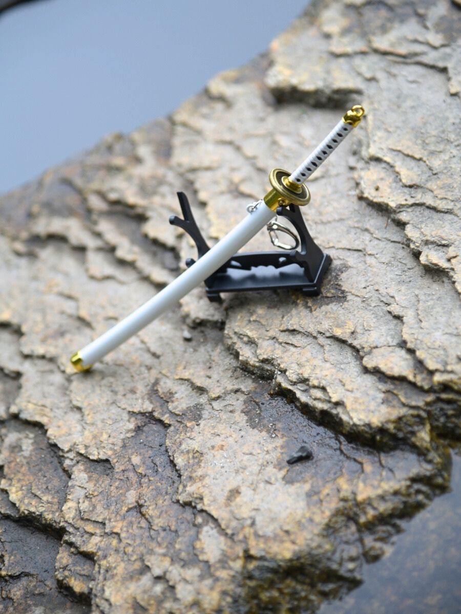 Diagonal top view of Ichimonji miniature katana halfway on its stand, set on a rock surrounded by water.