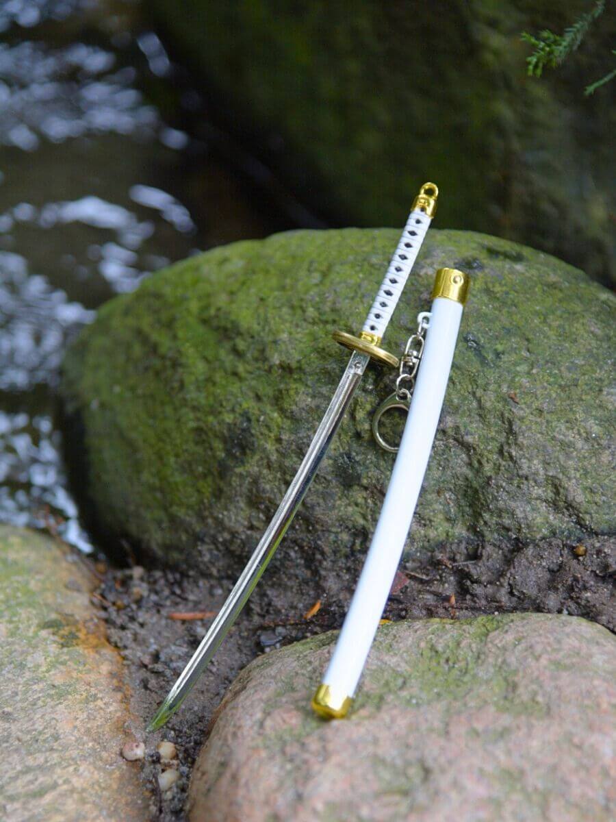 Ichimonji miniature katana and its sheath resting on a rock, surrounded by water.