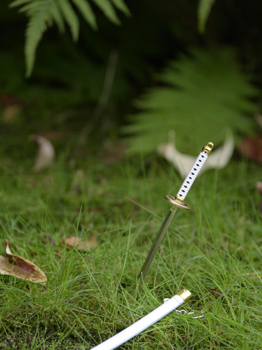 One Piece Ichimonji miniature katana thrust into the grass with its sheath lying beside.