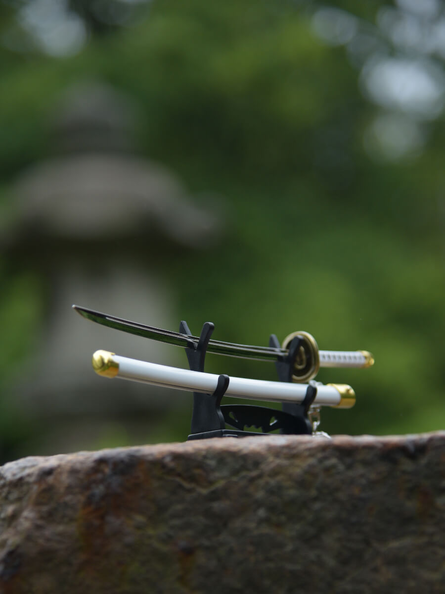 Ichimonji miniature katana on a stand, positioned on a rock, 45-degree blade-side view slightly from below.