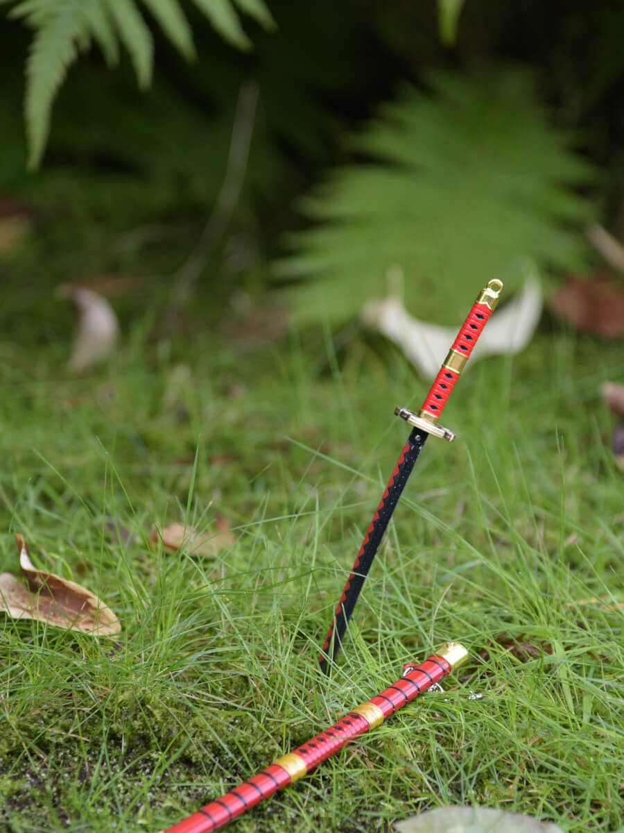 Kitetsu miniature katana from One Piece thrust into grass with its sheath laid beside.