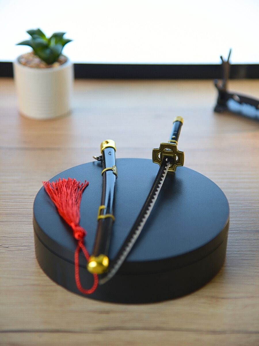 Bird's eye view of Zoro miniature katana, accompanied by its vibrant red sheath, laid out on a dark circular base, with a subtle cactus in the backdrop.
