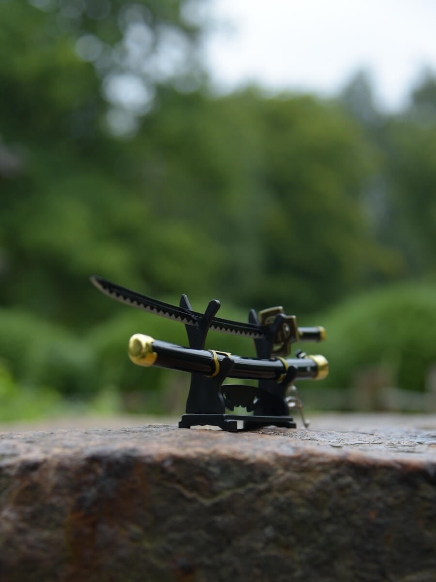 Dynamic 45-degree underside shot of Zoro miniature katana on its stand, stationed on a rugged rock, capturing its blade's brilliance.
