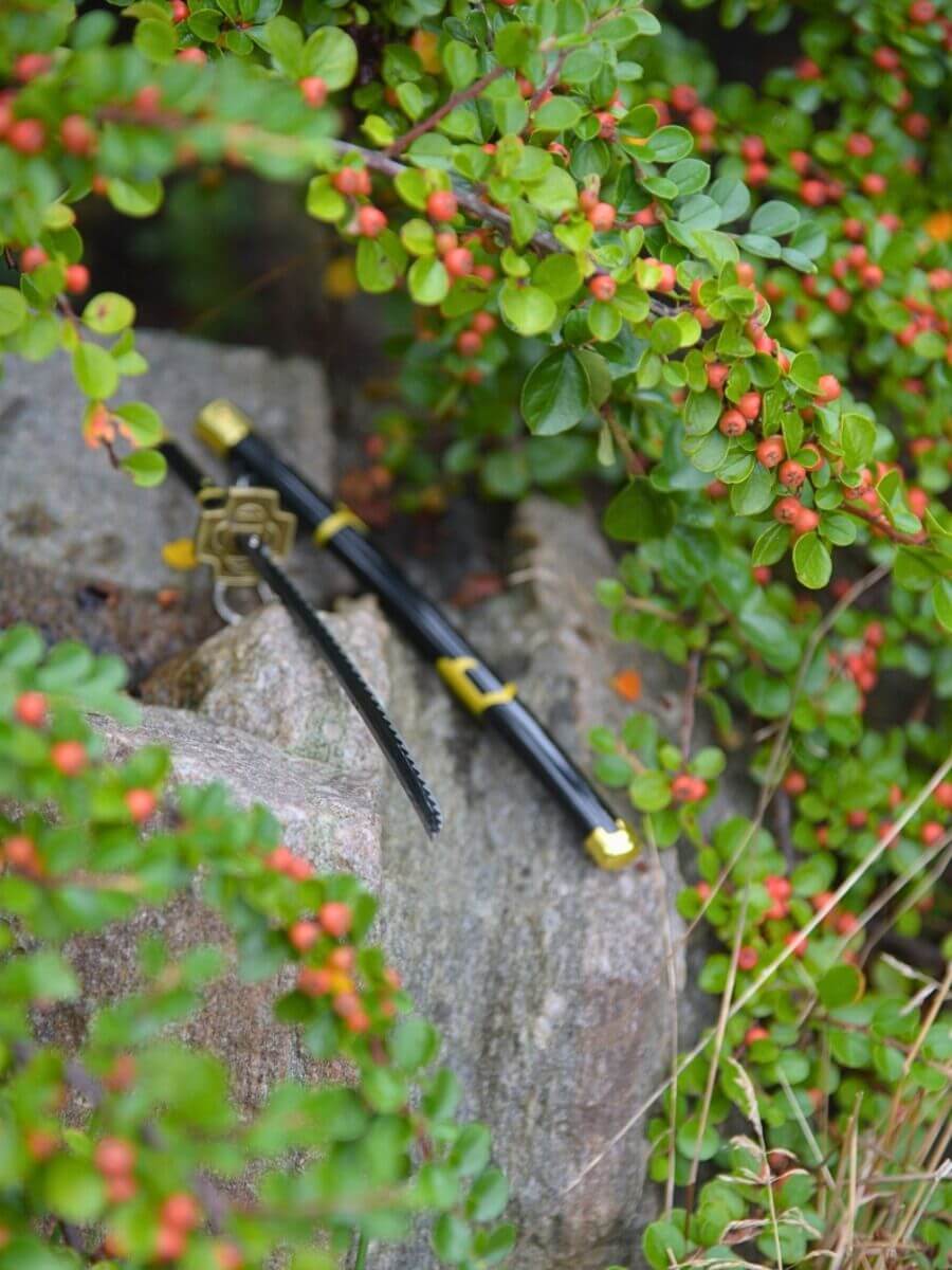 Tail-end view of Zoro miniature katana, lying amidst verdant flora on a stony surface, encapsulating nature's serenity.