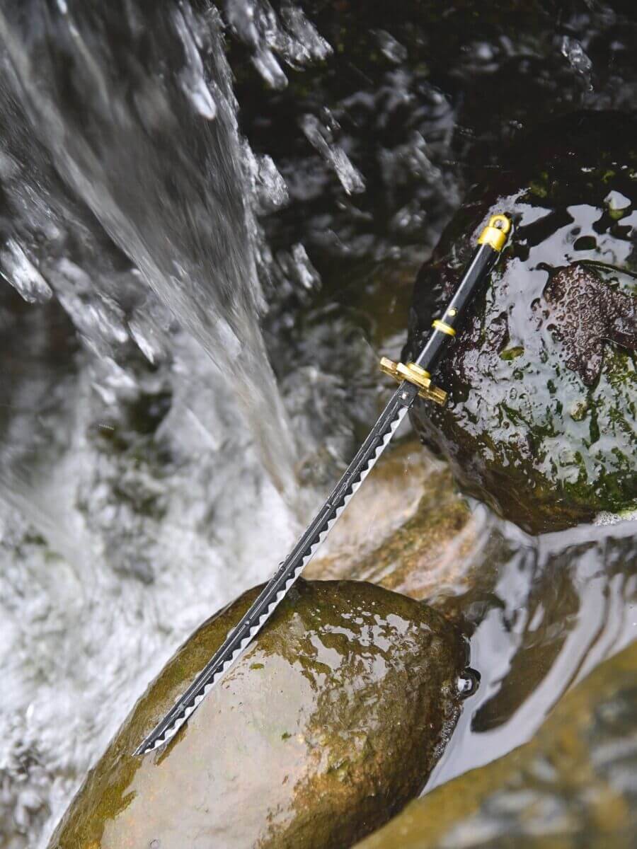Zoro miniature katana, positioned on a rocky terrain sprinkled with water droplets, hinting at a serene riverbed scene with a distant waterfall.