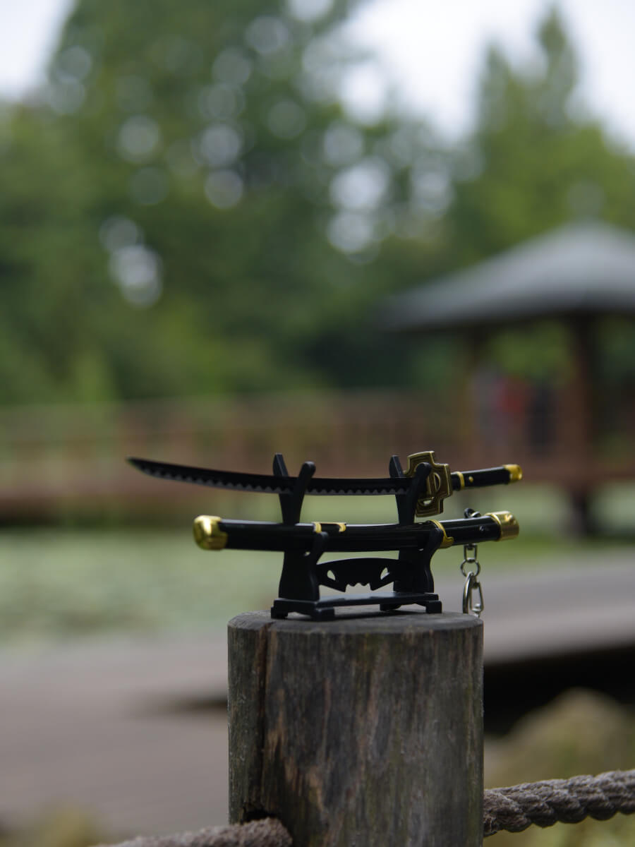 Zoro miniature katana showcased on its stand, erected on a wooden peg, with traditional Japanese architecture framing the backdrop.