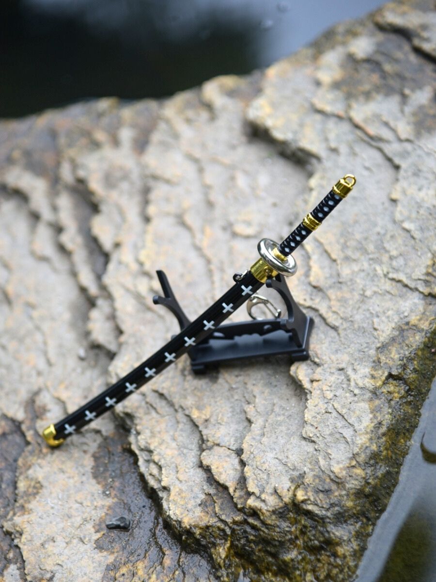 Diagonal, slightly top-down view of Trafalgar miniature katana on its stand, perfectly juxtaposed against a rock enveloped by water.