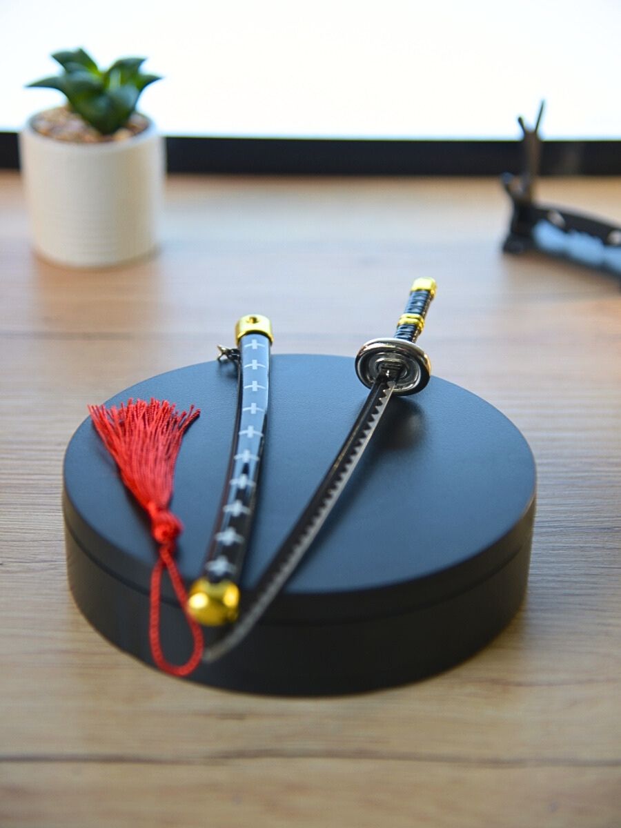 Trafalgar miniature sword and its distinct red scabbard from One Piece, showcased from a slightly overhead perspective on a black round base. A hint of home decor is given with a small cactus in the backdrop.