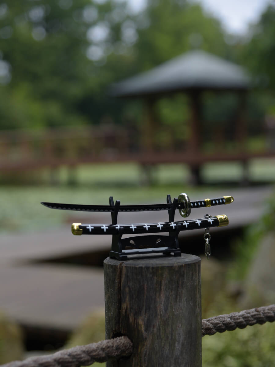 Trafalgar miniature katana from One Piece, proudly standing on a wooden peg stand. In the background, a traditional Japanese structure lends an authentic atmosphere.
