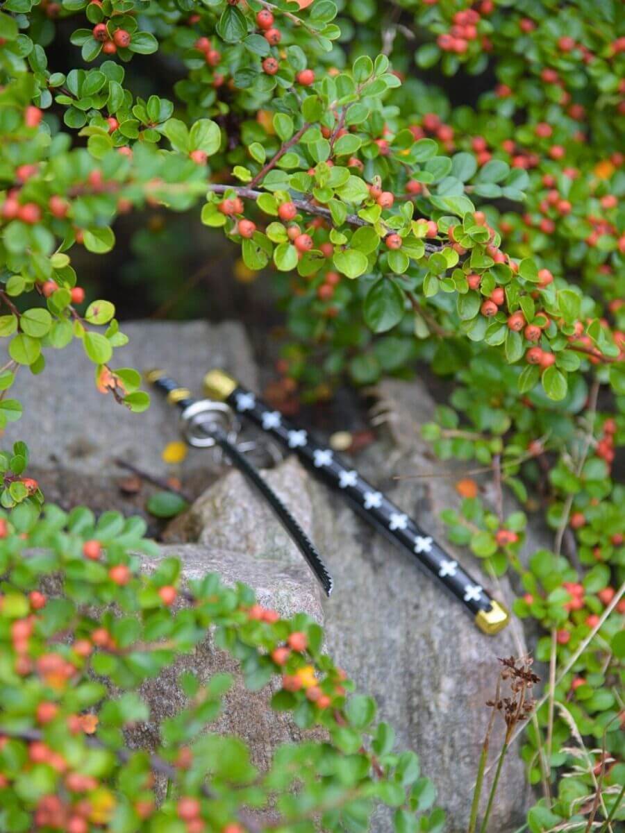 The sword tip of Trafalgar weapon miniature katana, resting amidst a rock setting, surrounded by lush greenery, suggesting harmony between warfare and nature.