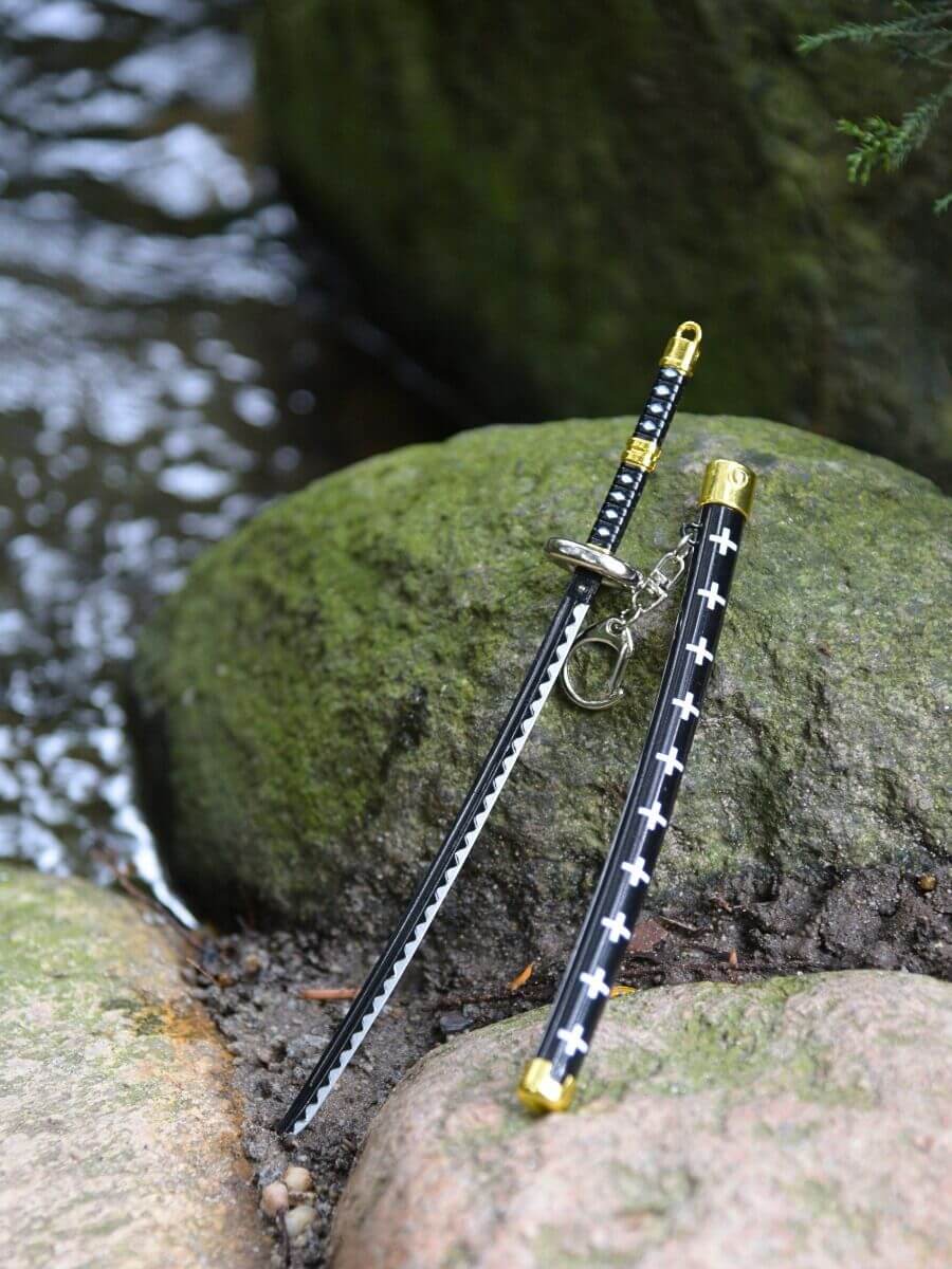 Trafalgar miniature katana, drawn out of its scabbard, lies peacefully on a rock, surrounded by a calming water setting.