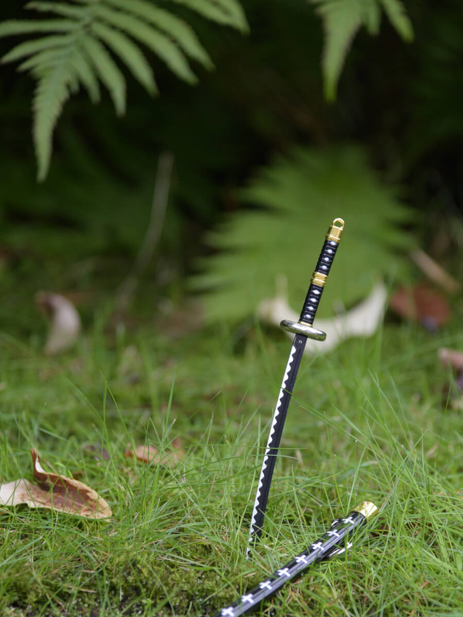 Trafalgar miniature katana from One Piece, thrust assertively into the grass, with its scabbard set aside, suggesting a moment of swift action.