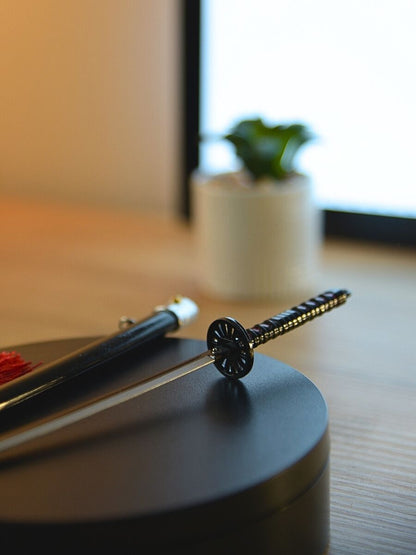 Detail of Tanjiro miniature katana hilt from Demon Slayer, focusing on the guard that protects the hand. Set on a black stand with a soft-focus cactus in the background for a personal touch.