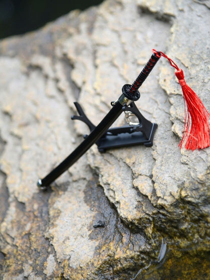 Top-down angled view of Tanjiro miniature katana on its stand, set on a rock surrounded by water, emphasizing the blend of weapon and nature.