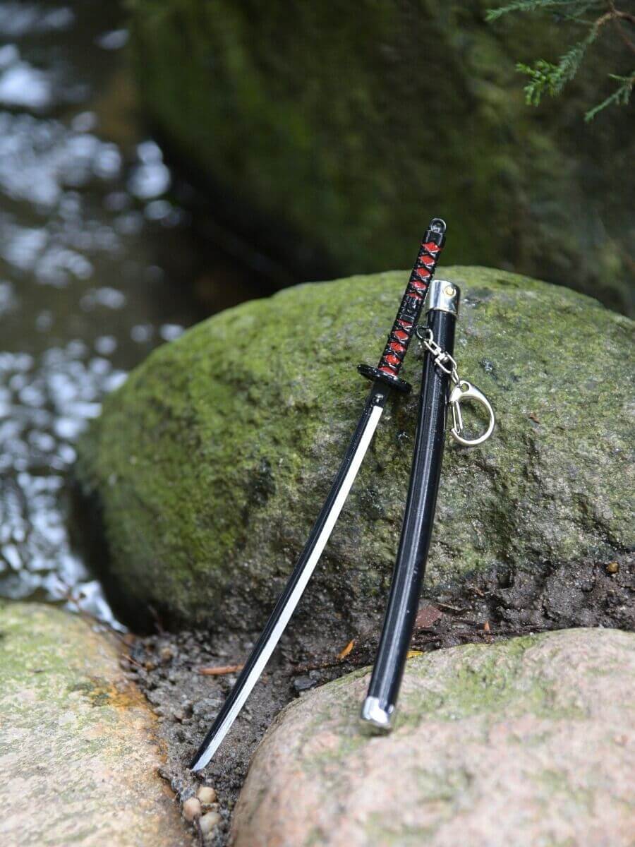 Tanjiro miniature katana, out of its scabbard, resting serenely on a rock with a watery environment surrounding it.