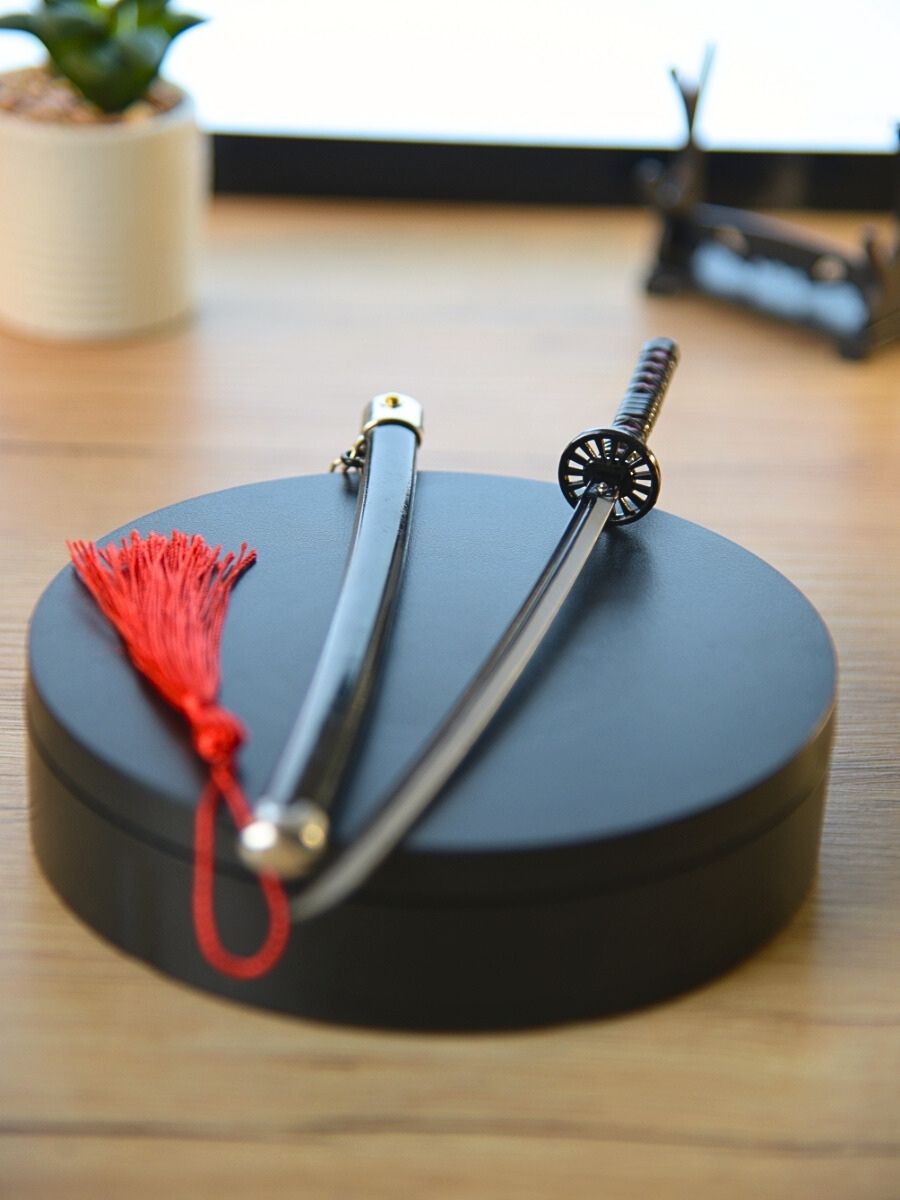 Tanjiro miniature katana and its red scabbard from Demon Slayer laid out on a black circular base. Overhead view with a small cactus in the backdrop for a hint of home ambiance.